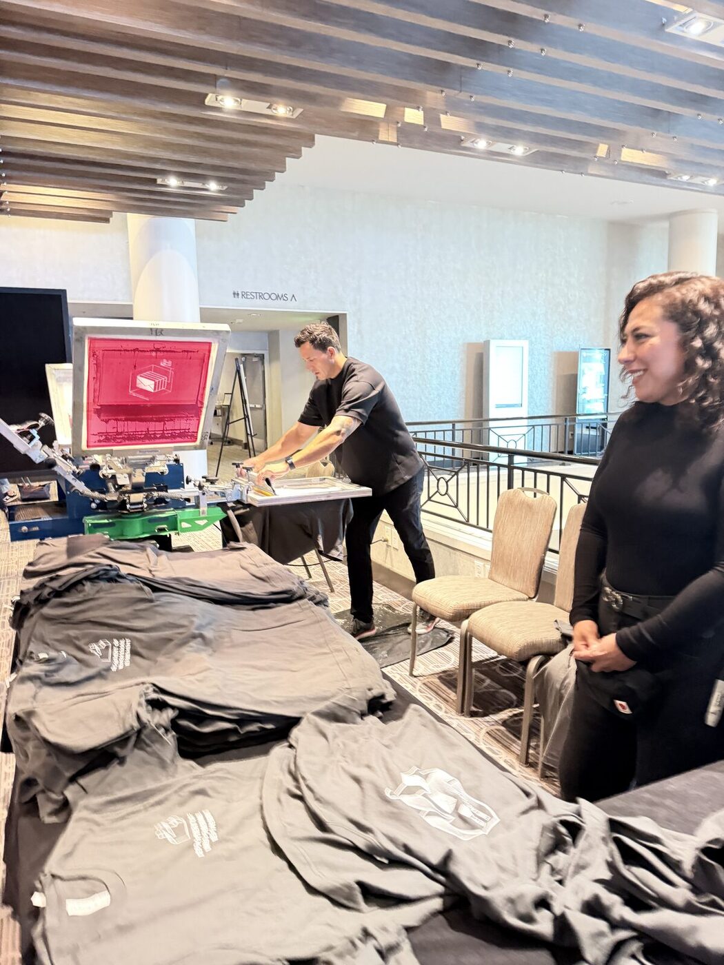 Crew pressing custom shirts on a hotel mezzanine with folded garments stacked in the foreground