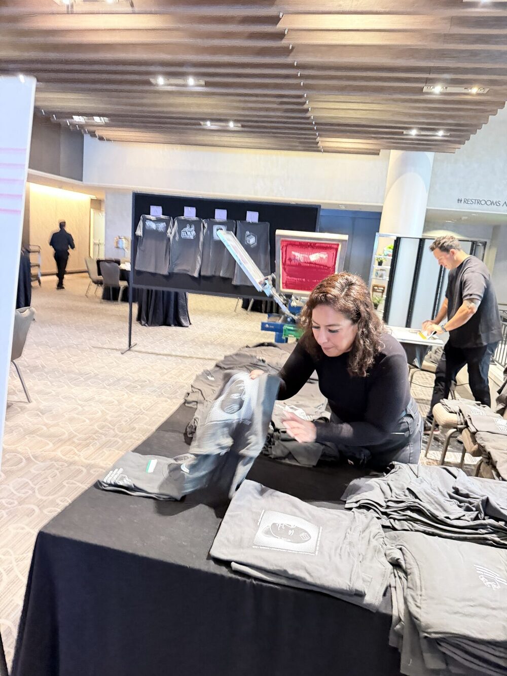 Crew member folding freshly printed event shirts on a table with a display rack behind