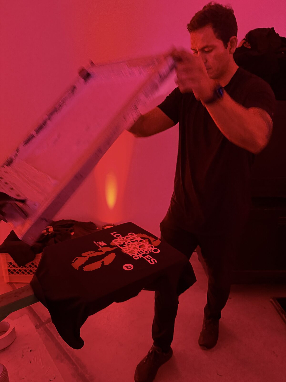 Printer lifting a frame to reveal a freshly printed shirt under red lighting at a launch party