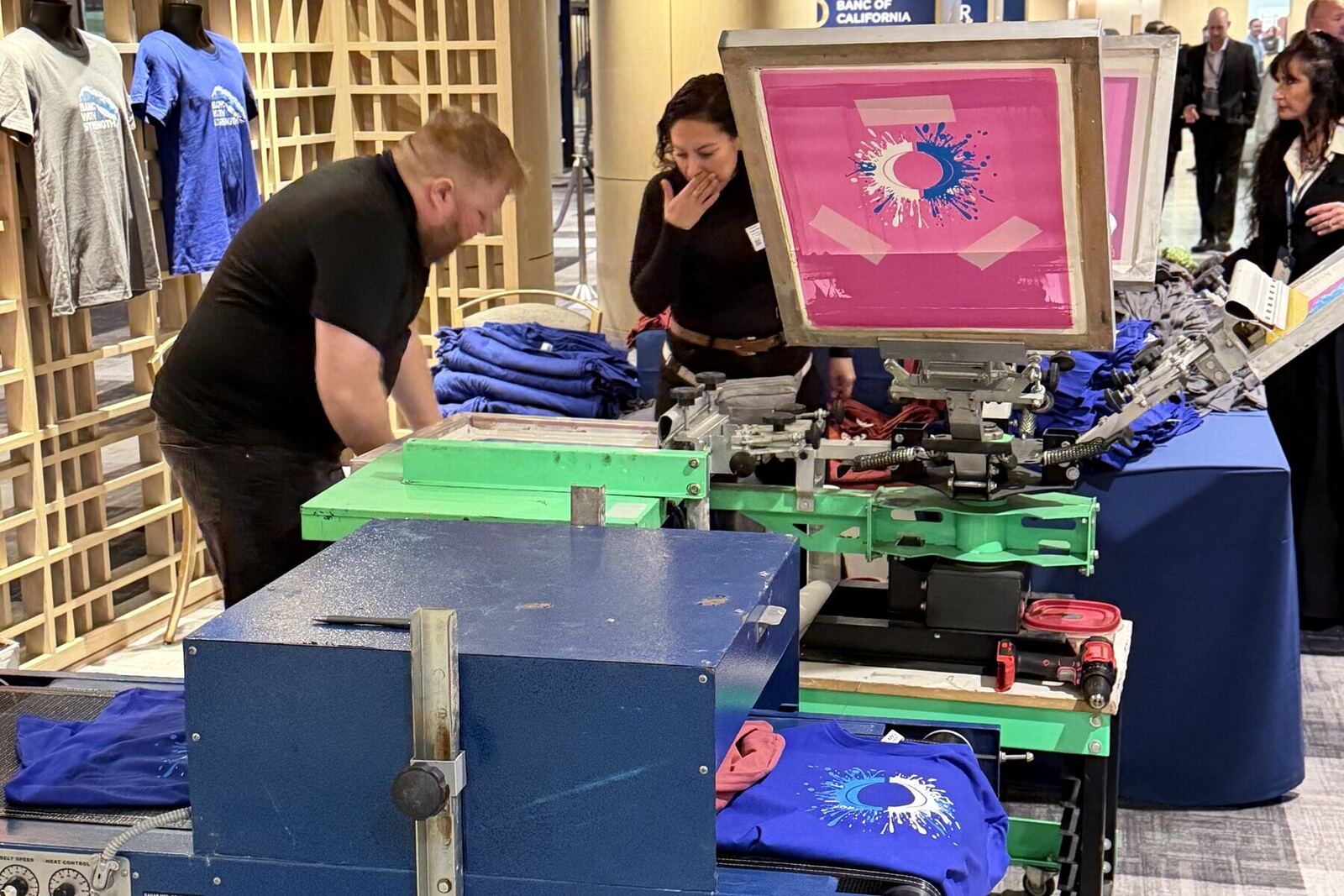 Merch Troop crew running a live garment printing station at a corporate conference with finished shirts displayed